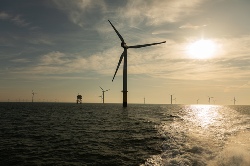 Offshore wind turbines in sea at dusk with substation in background