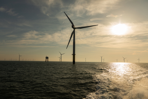 Offshore wind turbines in sea at dusk with substation in background